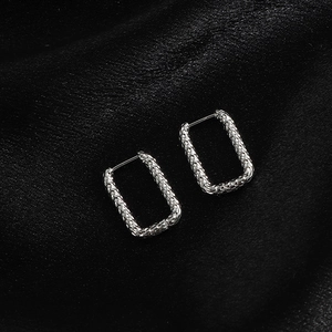 Gros plan de boucles d'oreilles rectangulaires argentées avec texture martelée sur satin