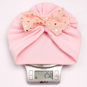 Pink infant turban hat with golden polka dot bow showing lightweight design at 25.8 grams