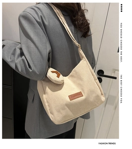 Detail of off-white corduroy tote bag worn over a grey blazer with letter A charm