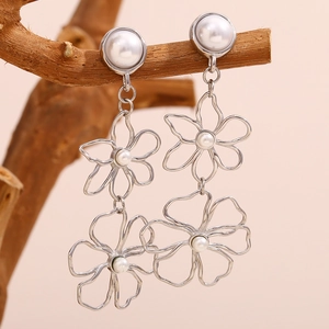Detail of silver floral earrings with pearls displayed on a natural wooden branch