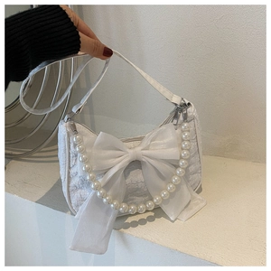 Close-up of stylish white handbag featuring a large silk bow and elegant pearl strap