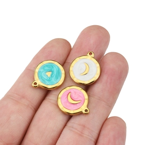 Hand holding golden stainless steel round pendants with moon and heart enamel patterns