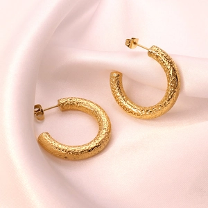 Vintage gold C-shaped textured earrings on silk background with a hammered metal finish