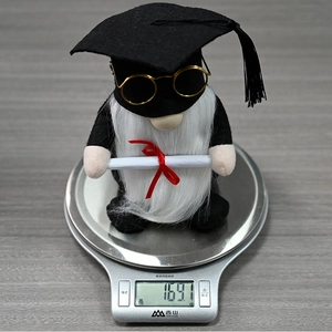 Close-up of a graduation gnome doll wearing glasses on a scale weighing 164.7g
