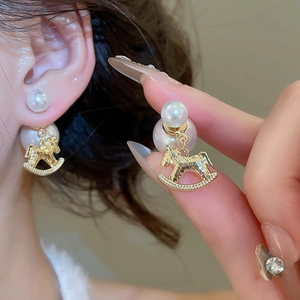 Detailed close-up of pearl and gold rocking horse earrings on a model's ear