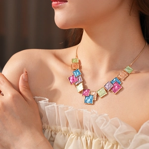 Close-up of golden necklace with colorful square pendants worn by a model in soft light