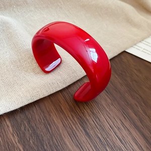 Bracelet jonc ouvert en acrylique rouge poli présenté sur une surface en bois