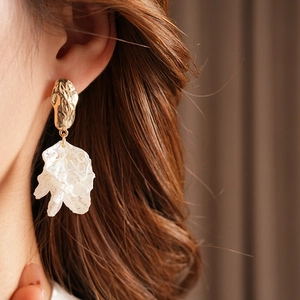 Detail of gold hammered metal and white layered petal earrings worn by a model