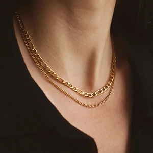 Detail of layered gold Figaro and curb chain necklaces worn on a model with a black top