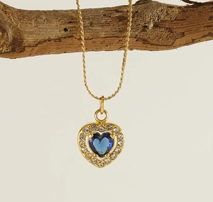Detail of a gold heart necklace with a blue gemstone on a rustic branch background