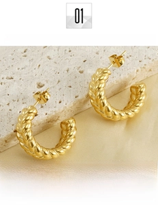 Macro detail of golden wheat-patterned twisted hoop earrings on soft silk fabric
