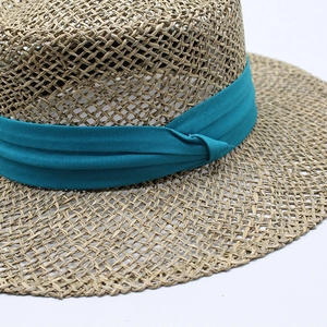 Detailed close-up of natural woven straw hat featuring a teal pleated fabric ribbon trim
