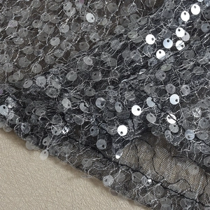 Gros plan de paillettes argentées sur tissu mesh noir pour haut de fête sans manches