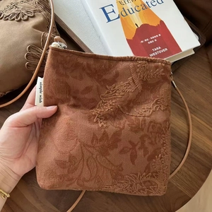 Détail du sac bandoulière brodé en daim camel présenté avec un livre sur table bois