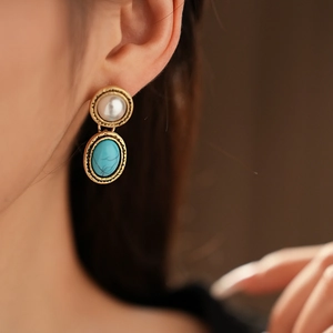 Close-up of vintage gold earrings with faux pearls and turquoise stones on model