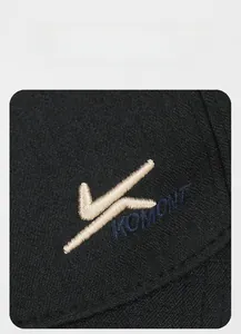 Macro shot of Komont logo with beige 3D embroidery on a black cotton baseball cap