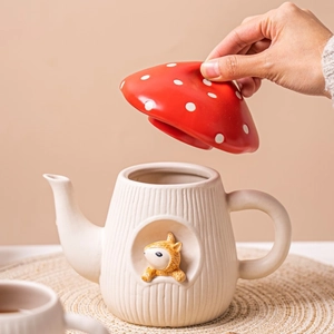 Detailed view of hand opening a red mushroom-shaped lid on a ceramic teapot with squirrel
