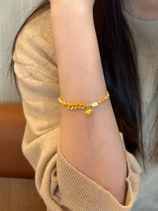 Detail of a vintage gold bracelet featuring coin textures and a small gourd charm on wrist