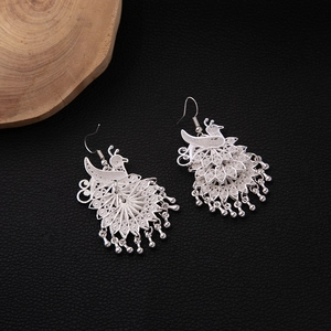 Detail of silver peacock earrings with intricate cutouts and dangling tassels on black leather