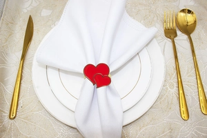 Close-up of red double heart napkin ring with gold trim on white fabric and gold cutlery