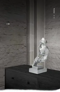 Detailed view of silver Silence is Gold sculpture placed on a modern dark wood cabinet