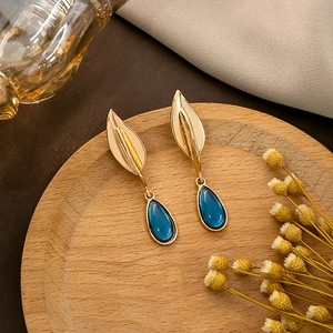 Bohemian gold leaf earrings with deep blue water drop pendants on a rustic wooden tray