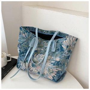 Detail of floral jacquard tote bag with blue faux leather strap on white platform
