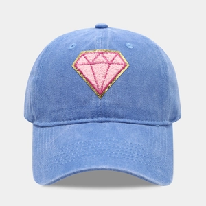 Detail of pink diamond embroidery on washed blue denim baseball cap with gold trim