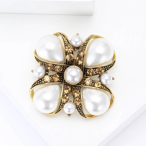 Elegant gold vintage brooch with large pearly petals and amber rhinestones on a white stand