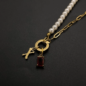 Close-up of gold stainless steel necklace with pearl chain, letter X and red gemstone