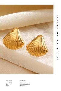 Detailed view of gold scallop shell earrings on textured stone with silk background
