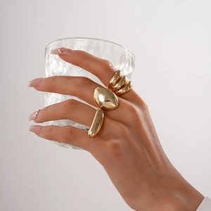 Close-up of chunky gold minimalist rings on a hand holding a textured glass