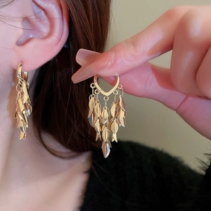 Detailed close-up of golden multi-layer leaf tassel earrings on a model with warm lighting