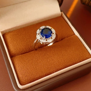 Detailed view of silver zircon flower ring with blue gemstone in orange velvet box