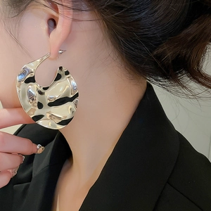 Detail of silver textured irregular metal earrings worn by a model in a side view