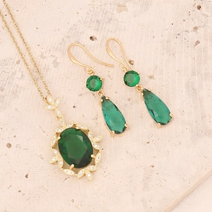 Detailed view of emerald green zircon pendant necklace and earrings on stone surface
