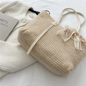 Straw tote bag with floral lace bow and faux leather straps on a white fabric background