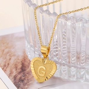Macro shot of gold heart-shaped pendant necklace with letter G engraving and fine chain