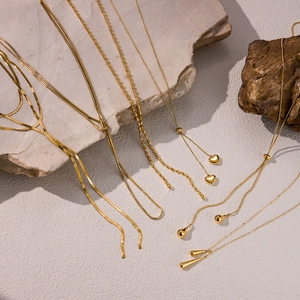 Detailed view of 5 golden stainless steel necklaces with heart and drop pendants on stone