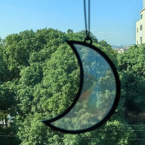 Detail of crescent moon glass suncatcher reflecting rainbow light against city window view