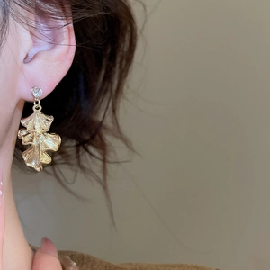 Close-up of golden ginkgo leaf earring with a sparkling zircon stud on model ear