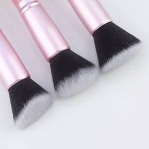 Macro detail of three professional makeup brushes with pink metal handles and soft dual-tone bristles