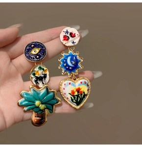 Macro view of asymmetrical surrealist enamel earrings with heart and eye motifs