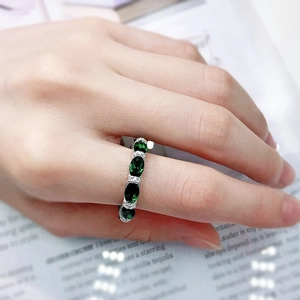 Close-up of a silver ring featuring oval green gemstones on a model's finger