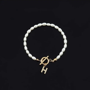 Elegant white oval pearl bracelet with golden H letter charm and rhinestone details