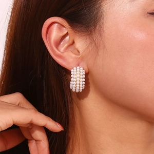 Close-up of pearl-encrusted 18K gold C-shaped hoop earrings worn by a model