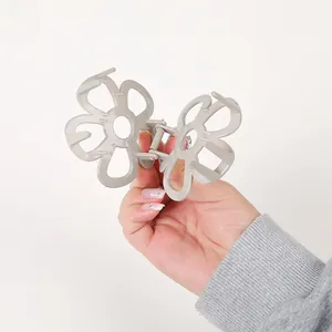 Detail of a matte grey flower hair claw clip with a hollow five-petal design held by hand