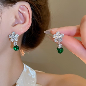 Macro shot of silver flower earrings with white zircons and a green round stone drop