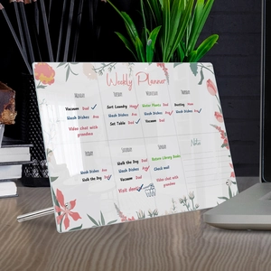 Clear acrylic weekly planner with floral patterns on a wooden desk with a metal stand