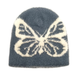 Macro detail of the fuzzy blue knit beanie featuring a large white butterfly jacquard pattern